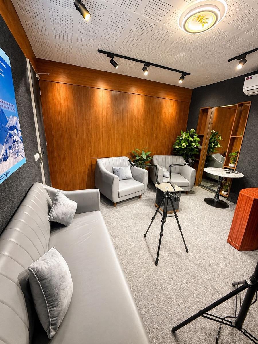 Interior of the podcast recording space in Ahmedabad showing acoustic ceiling treatment, track lighting, seating for four and a camera tripod